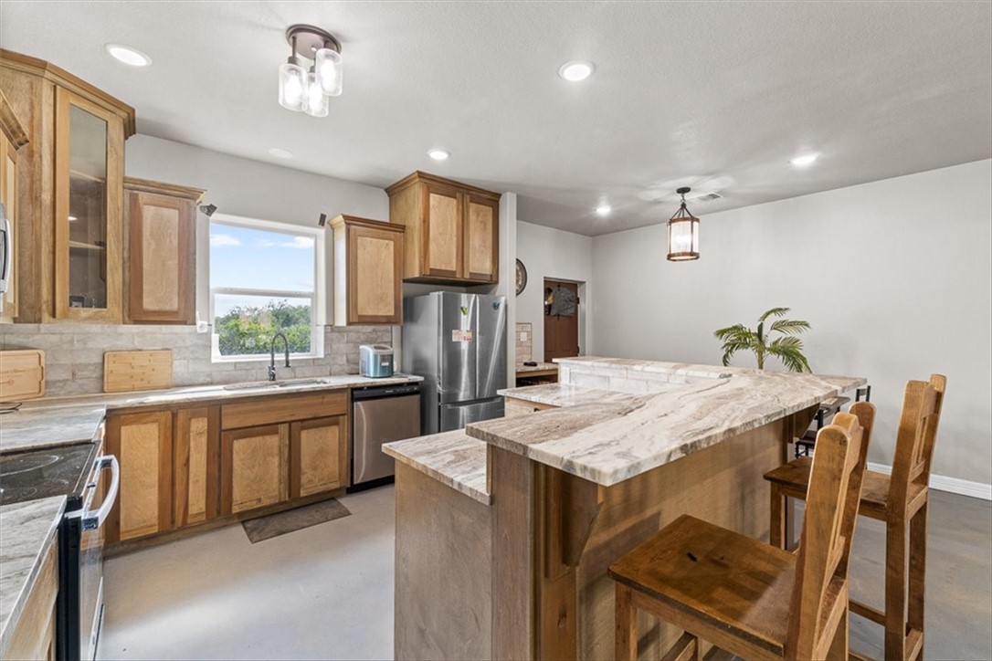 207 South Charles Street George West, TX 78022 - Photo 11 of 24 a kitchen with stainless steel appliances kitchen island granite countertop a table chairs in it and wooden floors