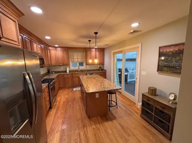 a kitchen with stainless steel appliances granite countertop a refrigerator a stove top oven a sink dishwasher and wooden cabinets with wooden floor