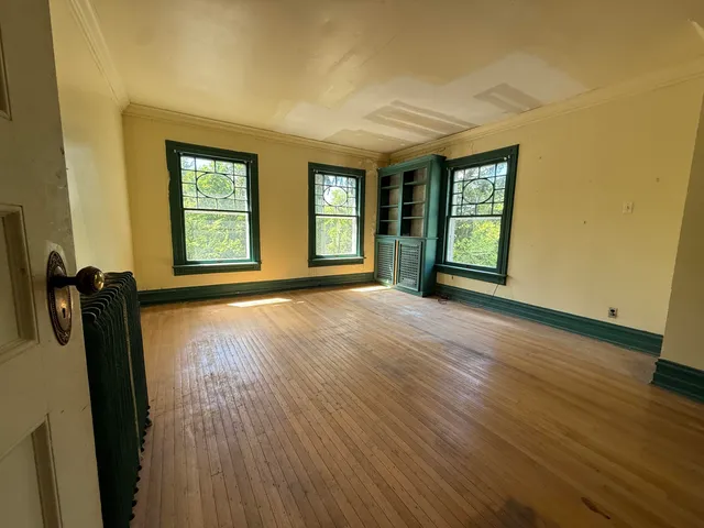 an empty room with wooden floor fireplace and windows