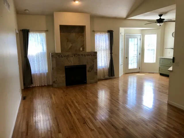 an empty room with wooden floor fireplace and windows
