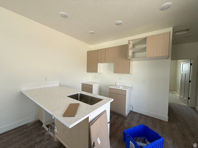 1008 West 3410 South Nibley, UT 84321 - Photo 23 of 26 Kitchen featuring a central island with an undermount stainless steel sink and light-toned countertop, upper and lower cabinetry with wood-finish doors, recessed ceiling lighting, and wood-finish flooring