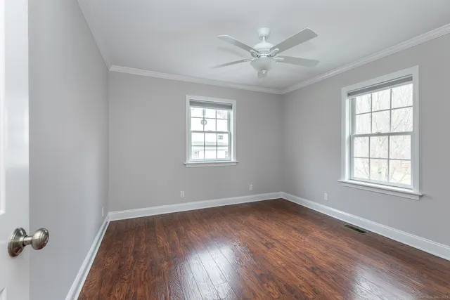 an empty room with wooden floor windows and fan