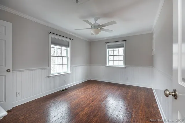 an empty room with wooden floor windows and fan