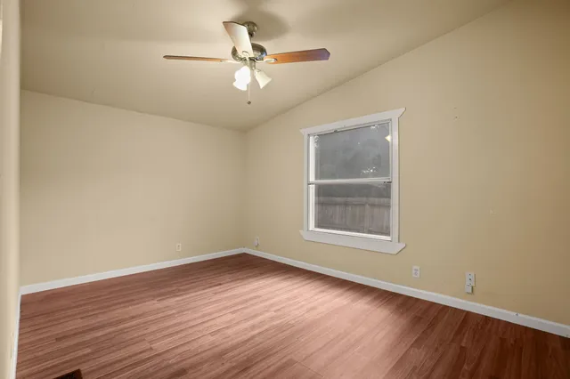 an empty room with wooden floor chandelier fan and windows
