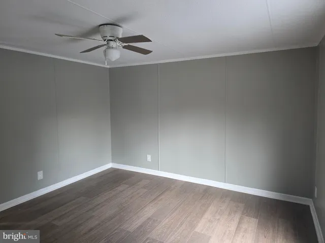 a view of an empty room with wooden floor and a ceiling fan