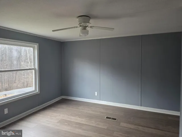 an empty room with wooden floor fan and windows