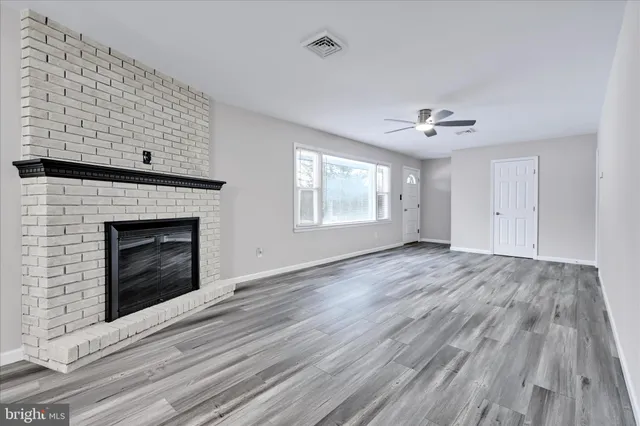 a view of an empty room with wooden floor fireplace and a window