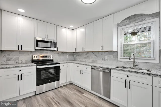 a kitchen with stainless steel appliances granite countertop white cabinets a sink a stove a microwave and wooden floors