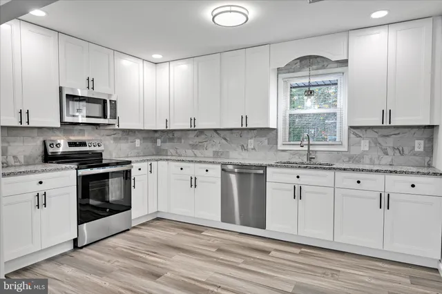a kitchen with granite countertop white cabinets white stainless steel appliances a sink and a window
