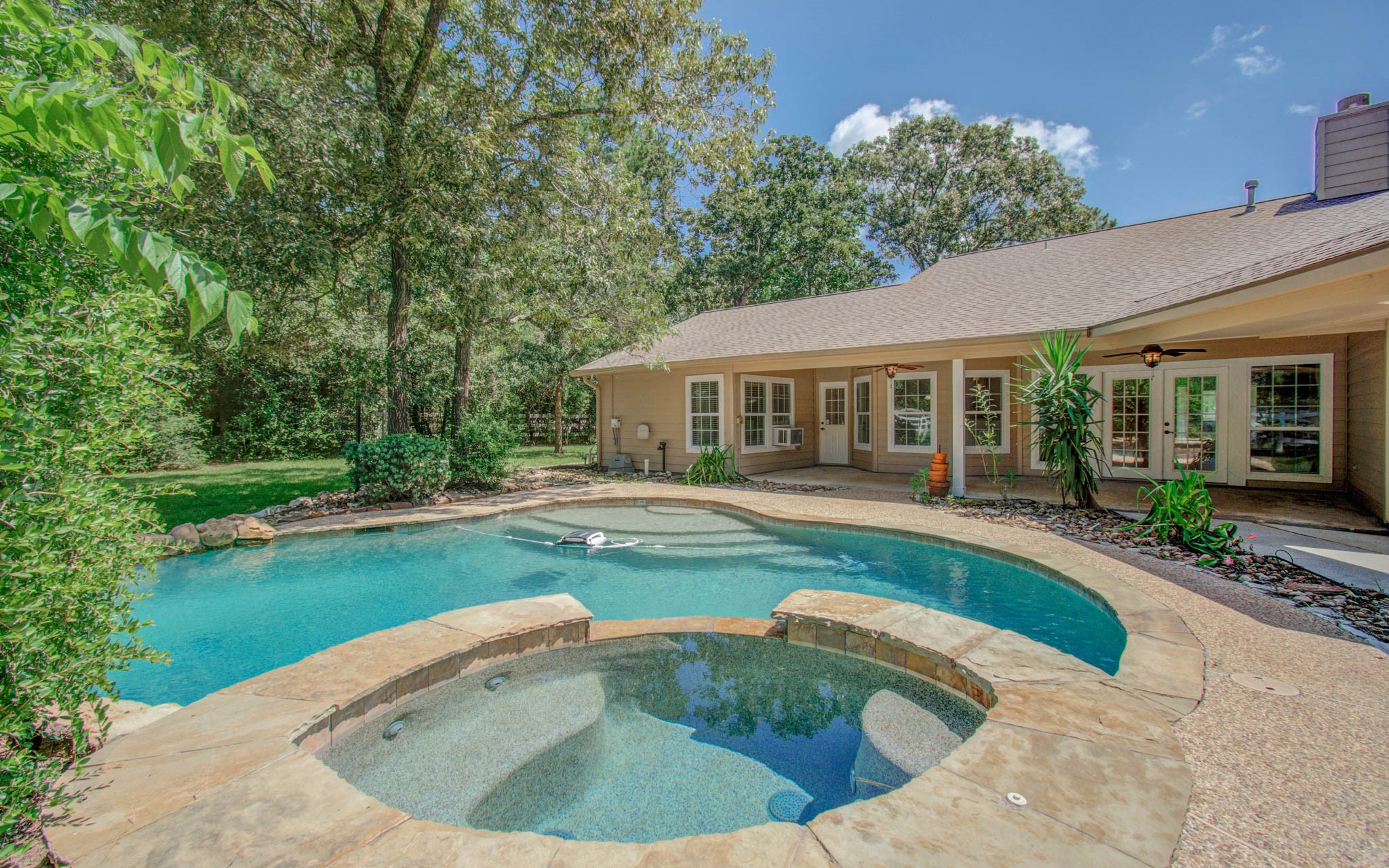 Beautiful backyard oasis with a freeform pool, attached spa, covered patio, and mature trees offering exceptional privacy. Ideal for entertaining or relaxing, this resort-inspired outdoor space combines lush landscaping with peaceful wooded views.