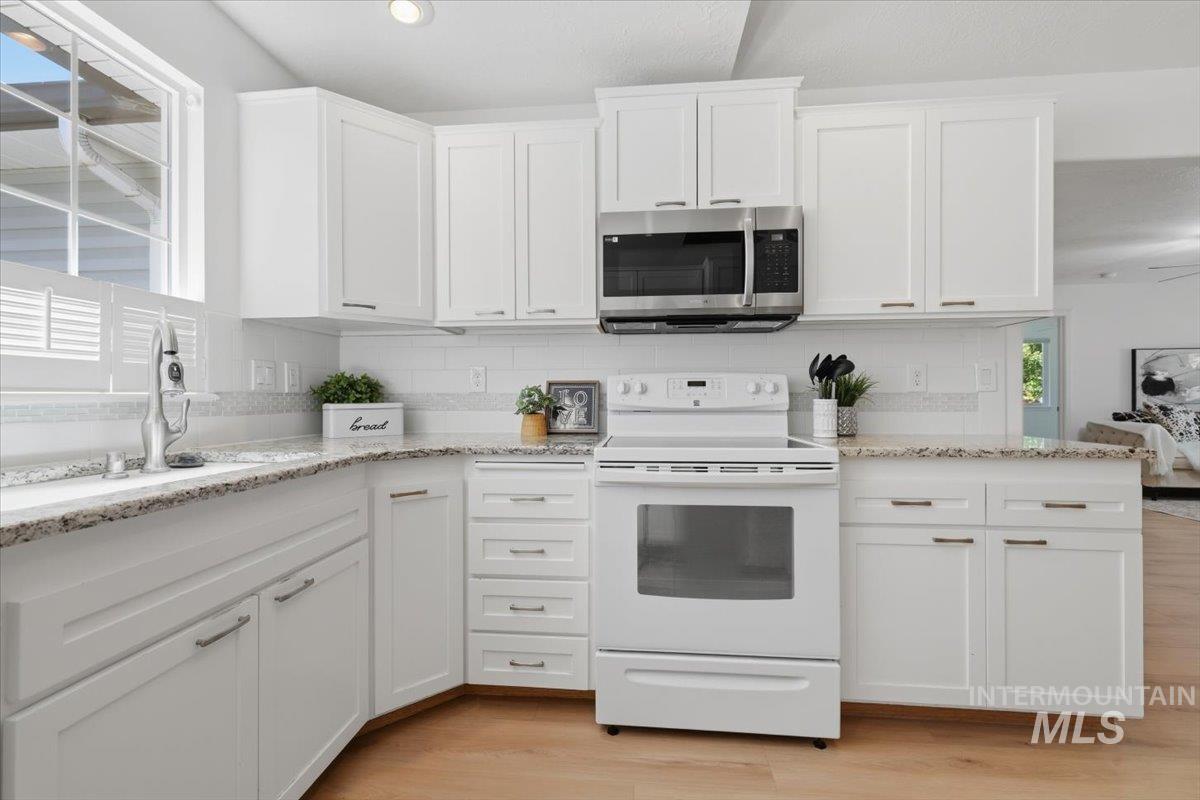 2075 North Springland Place Boise, ID 83713 - Photo 13 of 49 Kitchen featuring white shaker-style cabinetry, granite-finish countertops, subway tile backsplash, wood-finish flooring, and stainless steel microwave