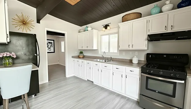 a kitchen with granite countertop a refrigerator a stove a sink and white cabinets with wooden floor