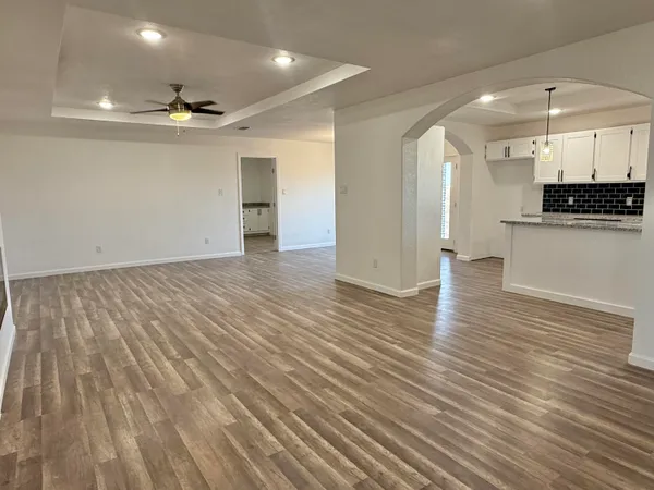 a view of an empty room with wooden floor and a kitchen