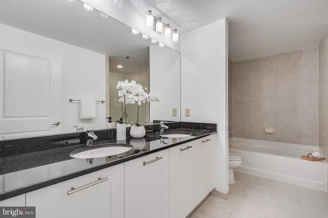 a bathroom with a granite countertop double vanity sink a mirror and a bathtub