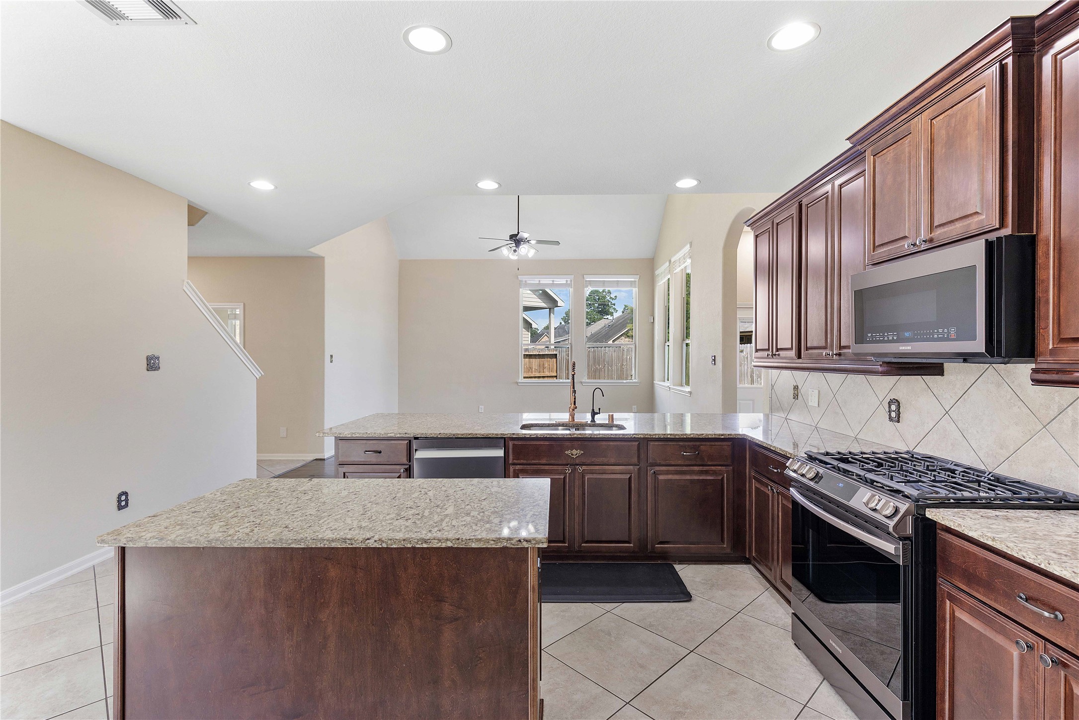 17206 Upper Ridge Lane Humble, TX 77346 - Photo 6 of 50 This kitchen features modern stainless steel appliances, rich wood cabinetry, and granite countertops. It's open to a bright living space with a ceiling fan and large windows, creating a welcoming atmosphere.