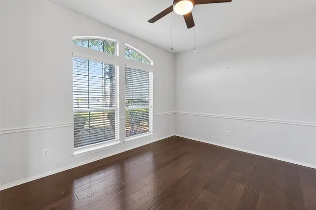 an empty room with wooden floor fan and windows