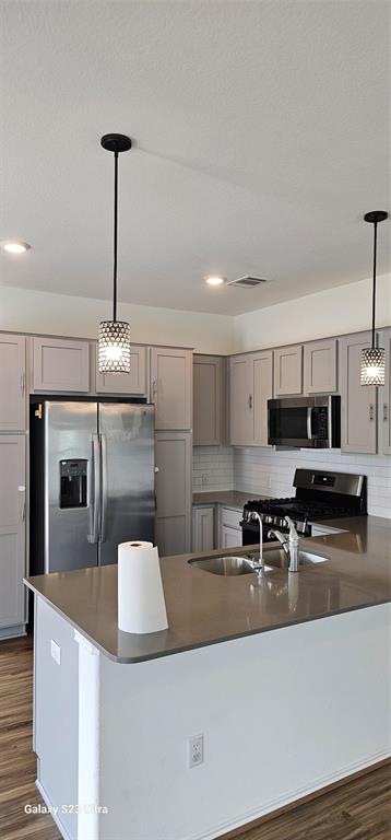 1401 Linwood Street Leander, TX 78641 - Photo 4 of 39 Kitchen featuring gray cabinets, appliances with stainless steel finishes, dark wood-style floors, decorative backsplash, and dark countertops