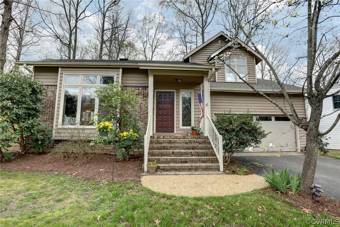 a view of a house with small yard plants and a large tree