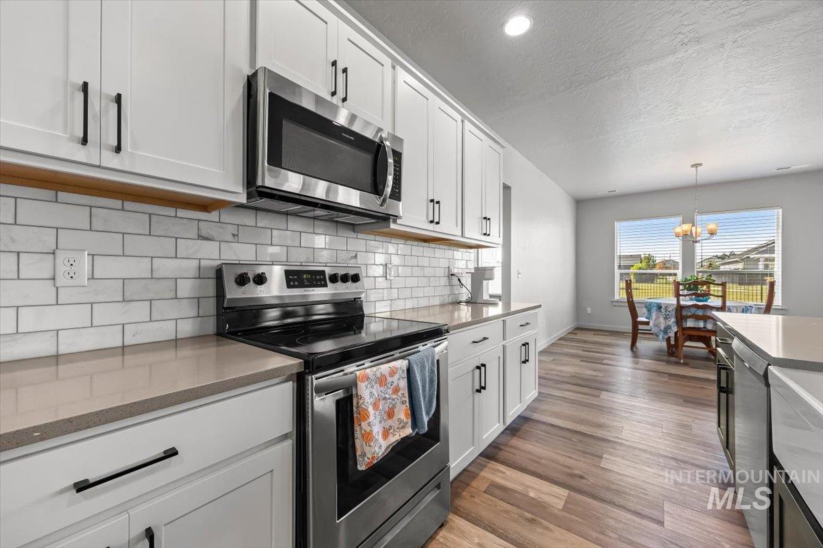 15365 Lutsen Avenue Caldwell, ID 83607 - Photo 21 of 42 Kitchen with stainless steel appliances, a textured ceiling, a chandelier, decorative backsplash, and white cabinetry
