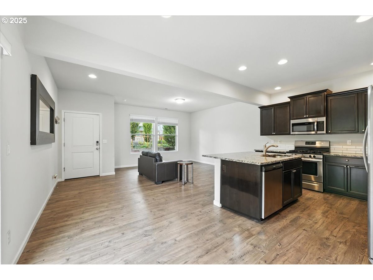 2103 Southeast 18th Alley Gresham, OR 97080 - Photo 3 of 25 a kitchen with stainless steel appliances kitchen island granite countertop a stove top oven a sink dishwasher a dining table and chairs with wooden floor