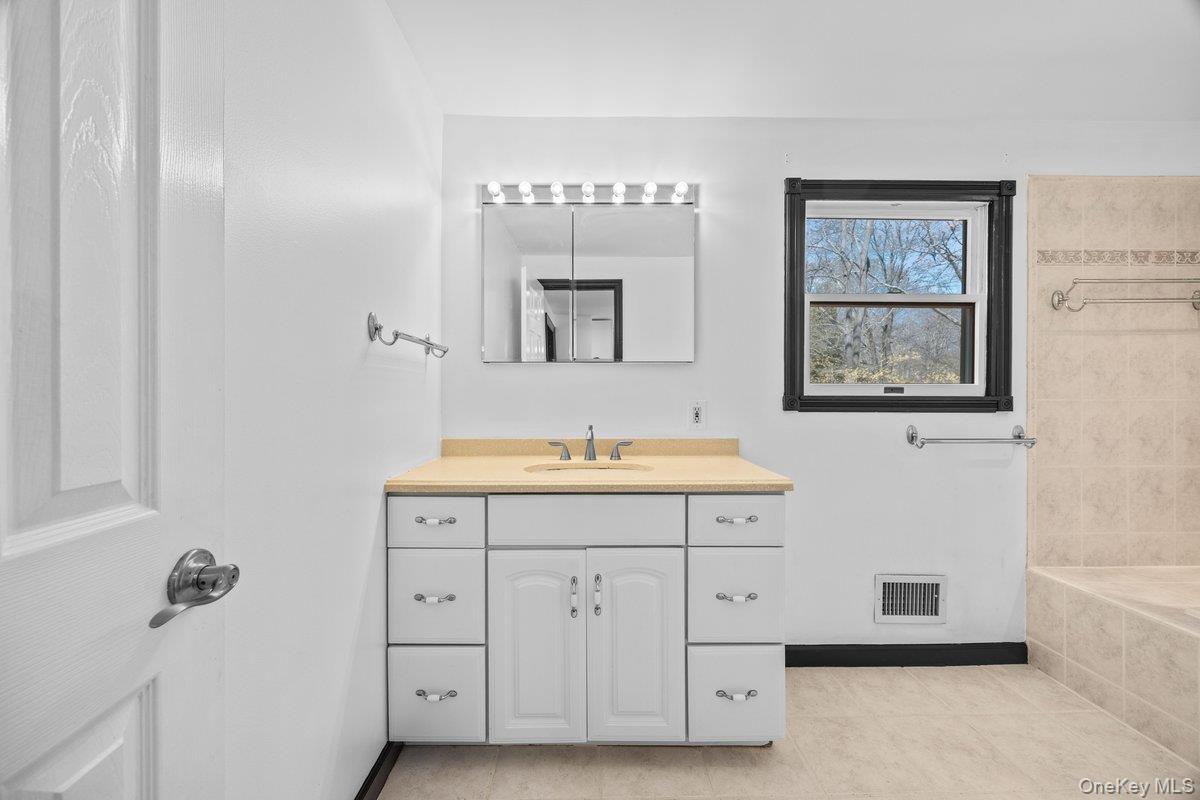 819 Canal Road Mount Sinai, NY 11766 - Photo 17 of 33 The bathroom features a vanity with a countertop, a sink, and cabinet storage, complemented by a lighted mirror