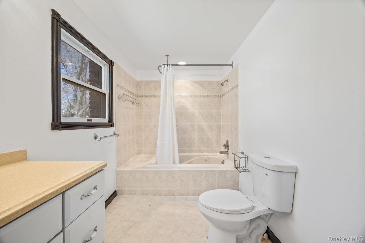 819 Canal Road Mount Sinai, NY 11766 - Photo 18 of 33 Bathroom featuring a window with dark trim, a tiled bath and shower combination, a toilet, and a vanity with a light-colored countertop