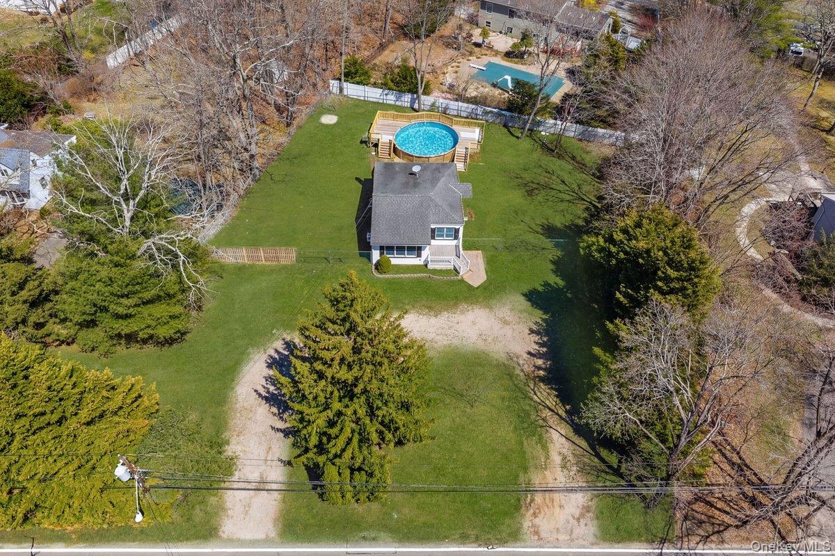 819 Canal Road Mount Sinai, NY 11766 - Photo 29 of 33 Aerial view of the property featuring a private above-ground pool with a surrounding deck, a well-maintained lawn, and mature trees