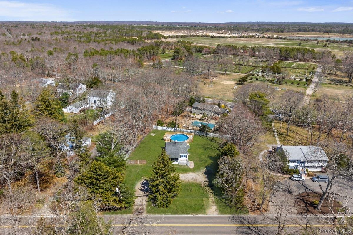 819 Canal Road Mount Sinai, NY 11766 - Photo 30 of 33 The property features a circular above-ground pool, a well-maintained lawn, and mature trees, all situated within a residential area surrounded by expansive wooded areas