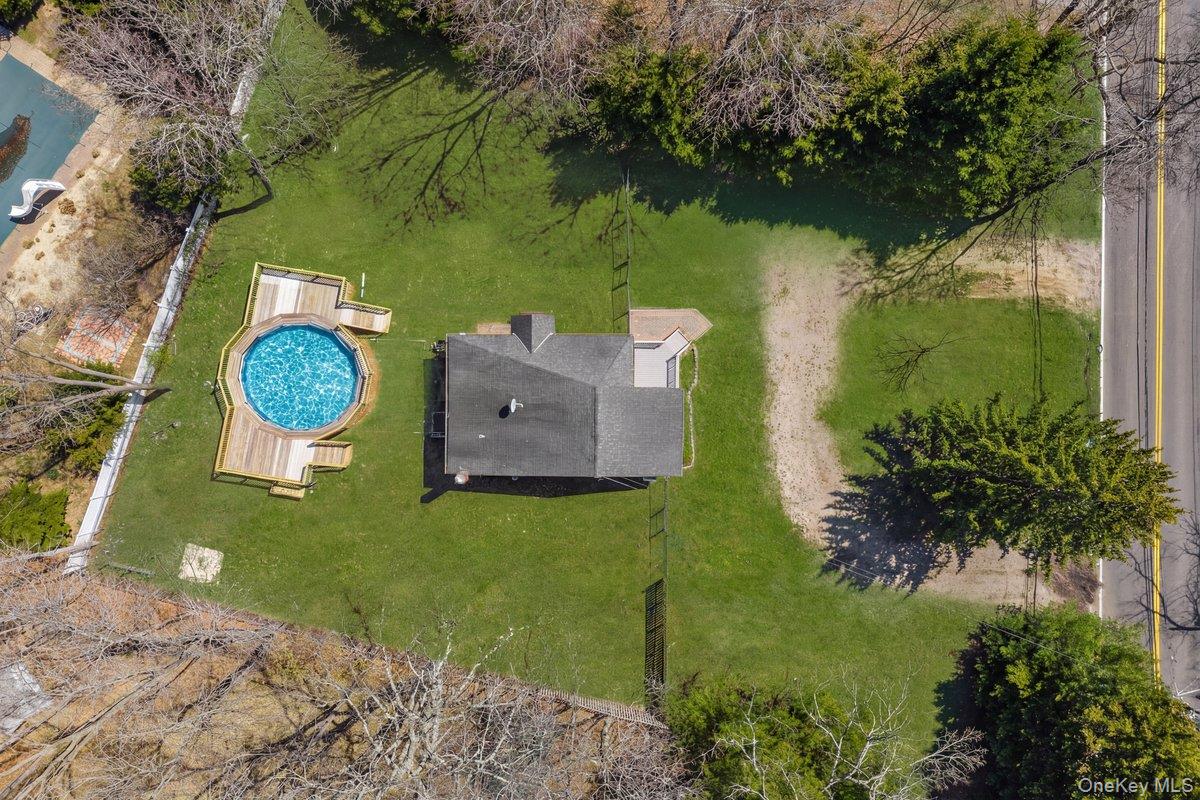 819 Canal Road Mount Sinai, NY 11766 - Photo 31 of 33 Aerial view of the property featuring a circular pool with an expansive wooden deck, a well-maintained lawn, and mature trees surrounding the perimeter