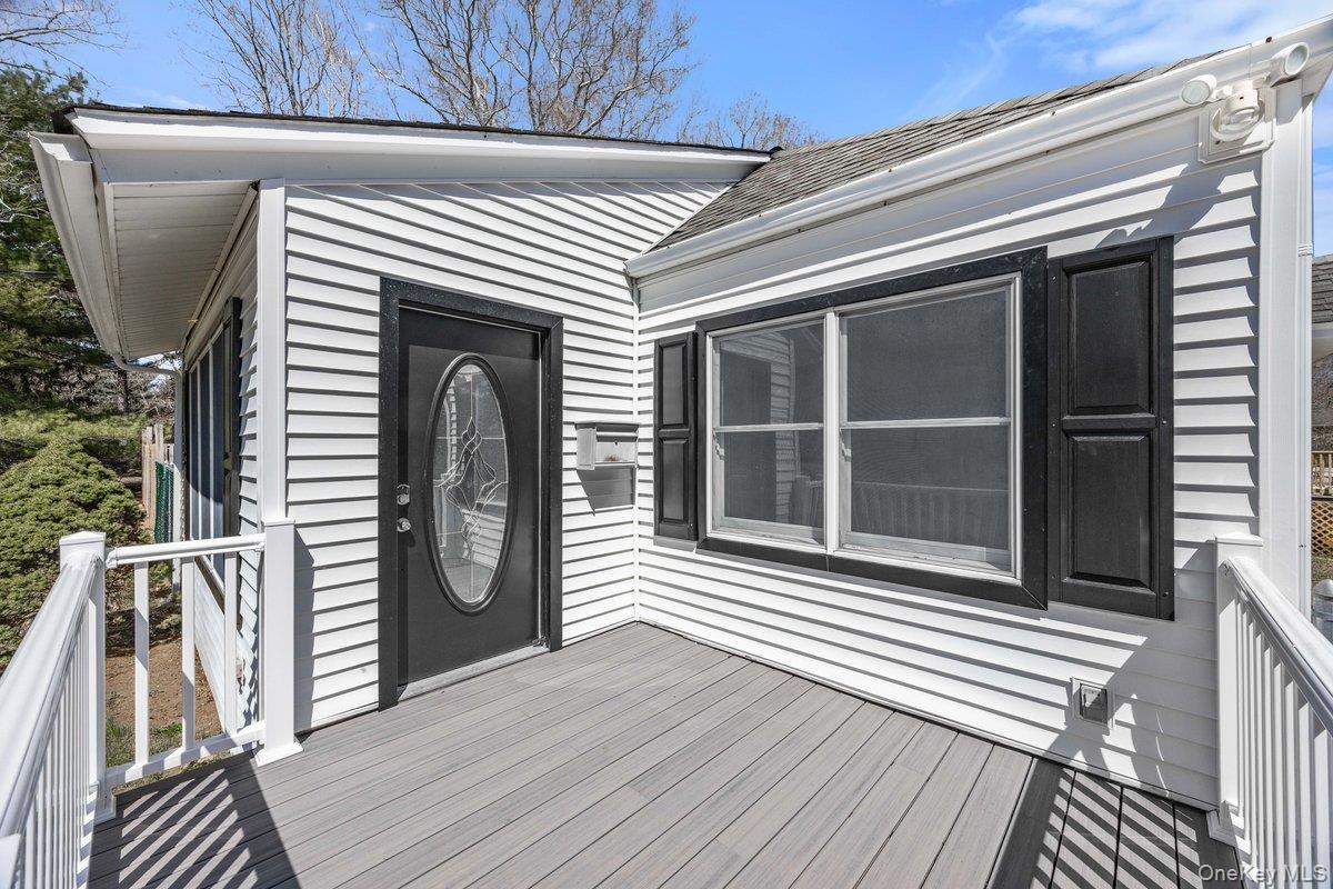 819 Canal Road Mount Sinai, NY 11766 - Photo 5 of 33 The property features white horizontal siding, a gray deck, and a black oval-lite front door