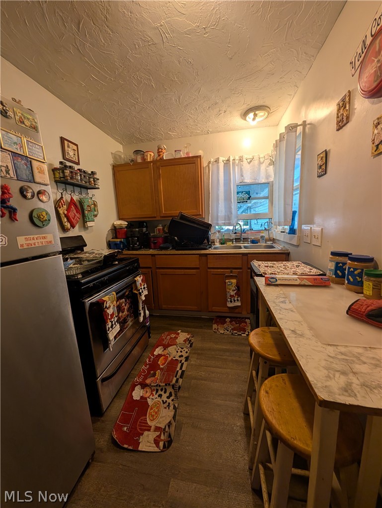 Compact kitchen featuring wood-finish cabinetry and a stainless steel refrigerator