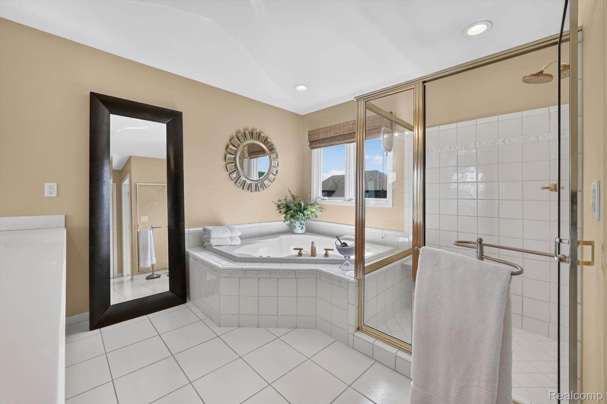 3804 Elk Drive Rochester, MI 48306 - Photo 40 of 75 Primary Bathroom featuring a tiled corner jetted tub, separate glass-enclosed shower with gold-tone fixtures, white square floor tiles, and a large window with privacy blinds