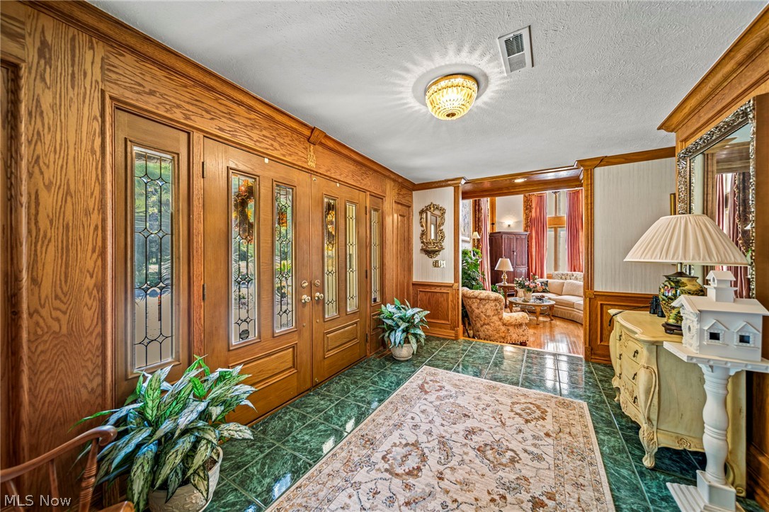 8801 Bunker Road Orwell, OH 44076 - Photo 7 of 50 Foyer featuring dark tile patterned floors, a textured ceiling, a wainscoted wall, and crown molding