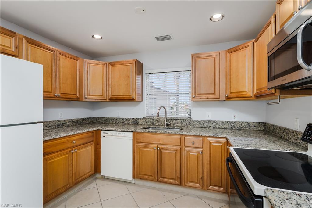 180 Cypress Way East, Unit B212 Naples, FL 34110 - Photo 12 of 40 a kitchen with stainless steel appliances granite countertop a sink stove and refrigerator