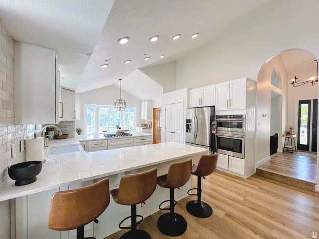12169 Hidden Valley Road, Unit 44 Sandy, UT 84092 - Photo 12 of 49 Kitchen featuring white cabinetry, quartz countertops, stainless steel appliances, wood-finish flooring, and vaulted ceilings