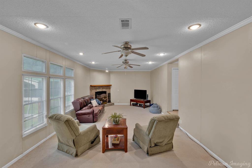 62 Princeton Lane Princeton, LA 71067 - Photo 24 of 33 Living area featuring ornamental molding, carpet flooring, a stone fireplace, a textured ceiling, and ceiling fan