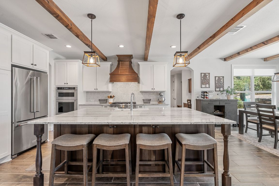 291 Southwick Ranch Road Johnson City, TX 78636 - Photo 13 of 40 Kitchen with beamed ceiling, white cabinets, light granite countertops, stainless steel appliances, and dark wood-tile flooring
