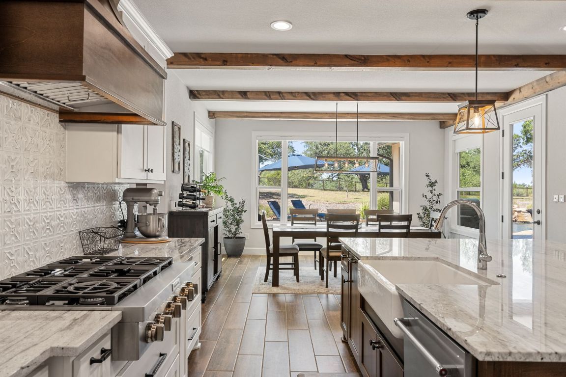 291 Southwick Ranch Road Johnson City, TX 78636 - Photo 14 of 40 Kitchen with light stone counters, appliances with stainless steel finishes, hanging light fixtures, premium range hood, and beamed ceiling