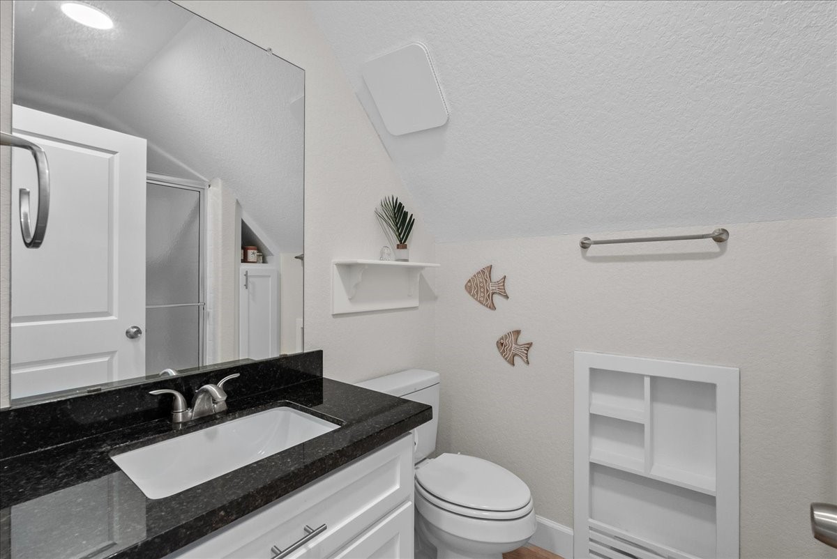 130 Beachcomber Avenue Surfside Beach, TX 77541 - Photo 18 of 33 This is a compact, stylish bathroom featuring a sleek granite countertop, white cabinetry, and modern fixtures. The space includes a shower, decorative wall elements, and shelving for storage, all set against a neutral color palette.