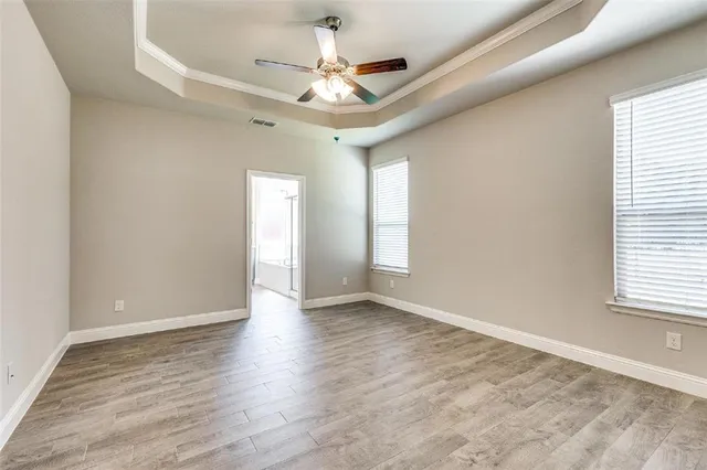 an empty room with wooden floor chandelier fan and windows