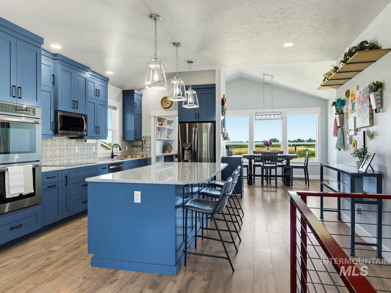 4950 West Columbia Road Nampa, ID 83687 - Photo 11 of 50 Modern kitchen featuring blue cabinetry, built-in stainless steel appliances, a white speckled countertop island with pendant lighting, and wood-finish flooring extending into the dining area