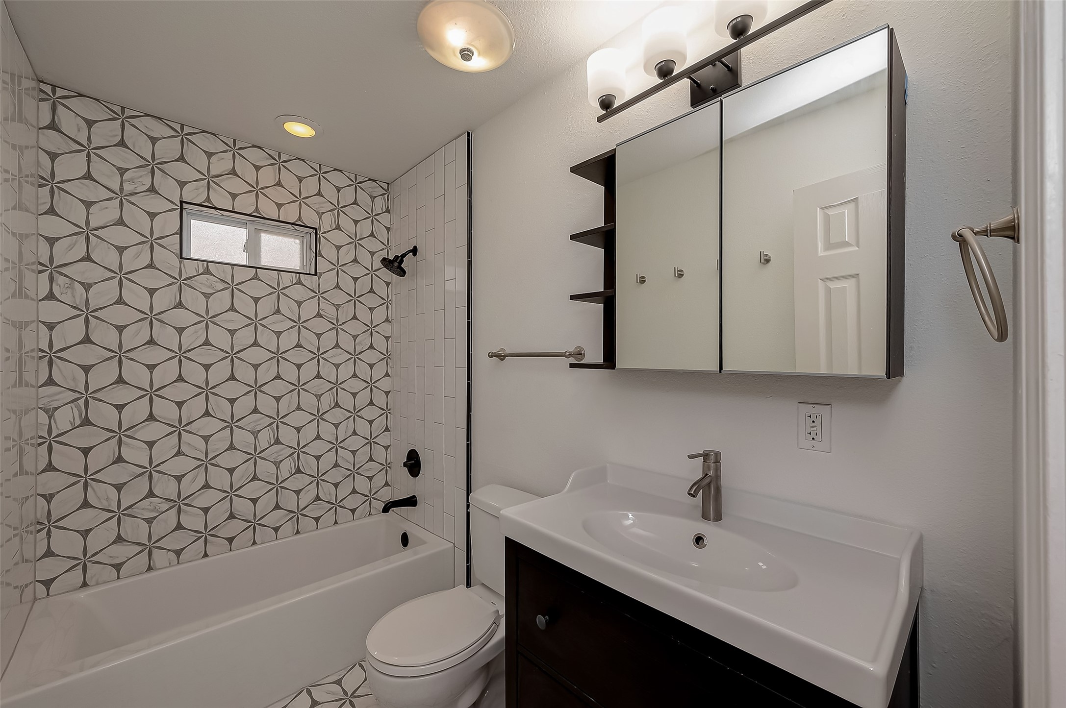 917 Adele Street Houston, TX 77009 - Photo 18 of 24 Remodeled in 2024, the bathroom features a stunning patterned tile surround, modern vanity, and mirrored medicine cabinet.