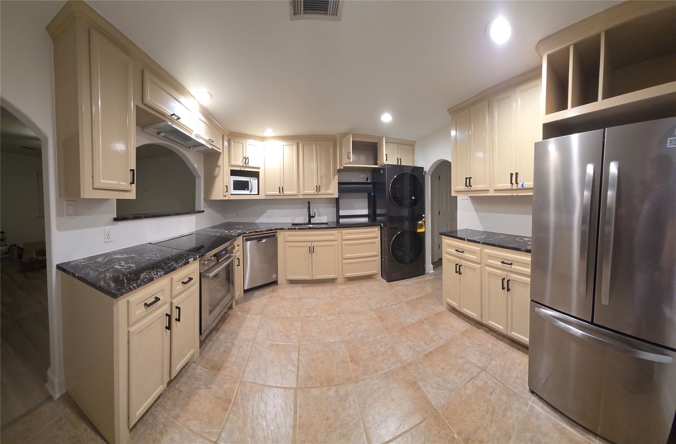 917 Adele Street Houston, TX 77009 - Photo 8 of 24 Brand-new 2026 appliances throughout: Bosch induction range, stainless dishwasher, French door refrigerator, microwave, and stacked LG ThinQ washer/dryer. Dark granite countertops and cream cabinetry complete the space.