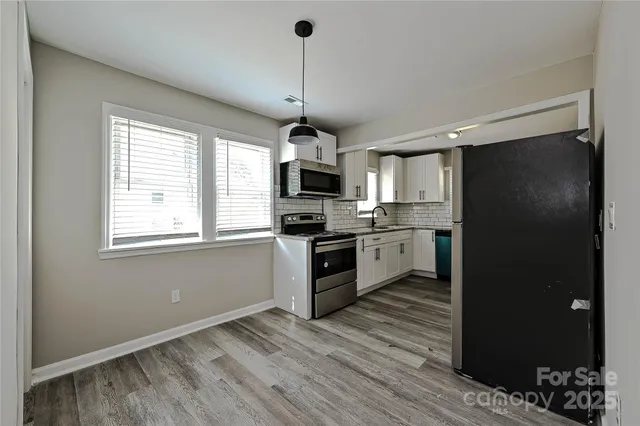 a kitchen with granite countertop stainless steel appliances a refrigerator cabinets and a wooden floor