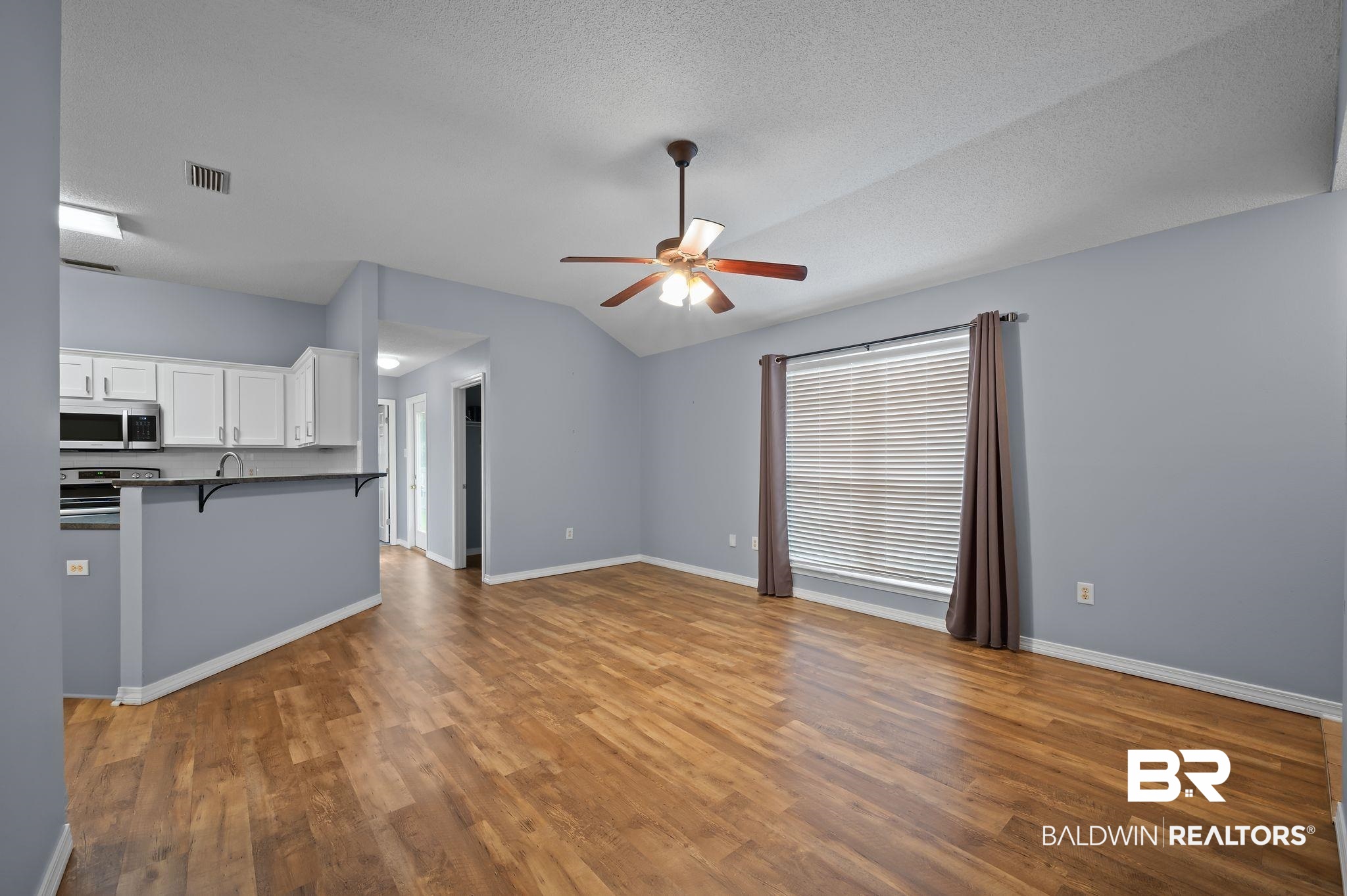 8901 Fall Court Mobile, AL 36695 - Photo 4 of 23 Unfurnished living room featuring vaulted ceiling, a ceiling fan, wood finished floors, and a textured ceiling