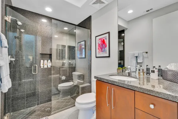 a bathroom with a granite countertop sink a toilet a shower and a mirror