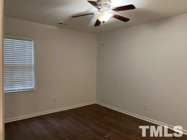 an empty room with wooden floor fan and windows