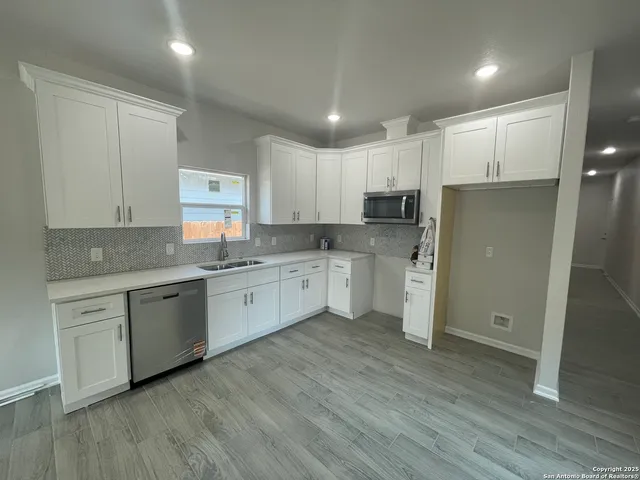 a kitchen with a white cabinets a sink a window and stainless steel appliances