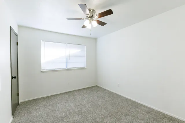 an empty room with a chandelier fan and windows