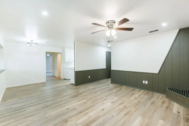 a view of an empty room with wooden floor and a ceiling fan